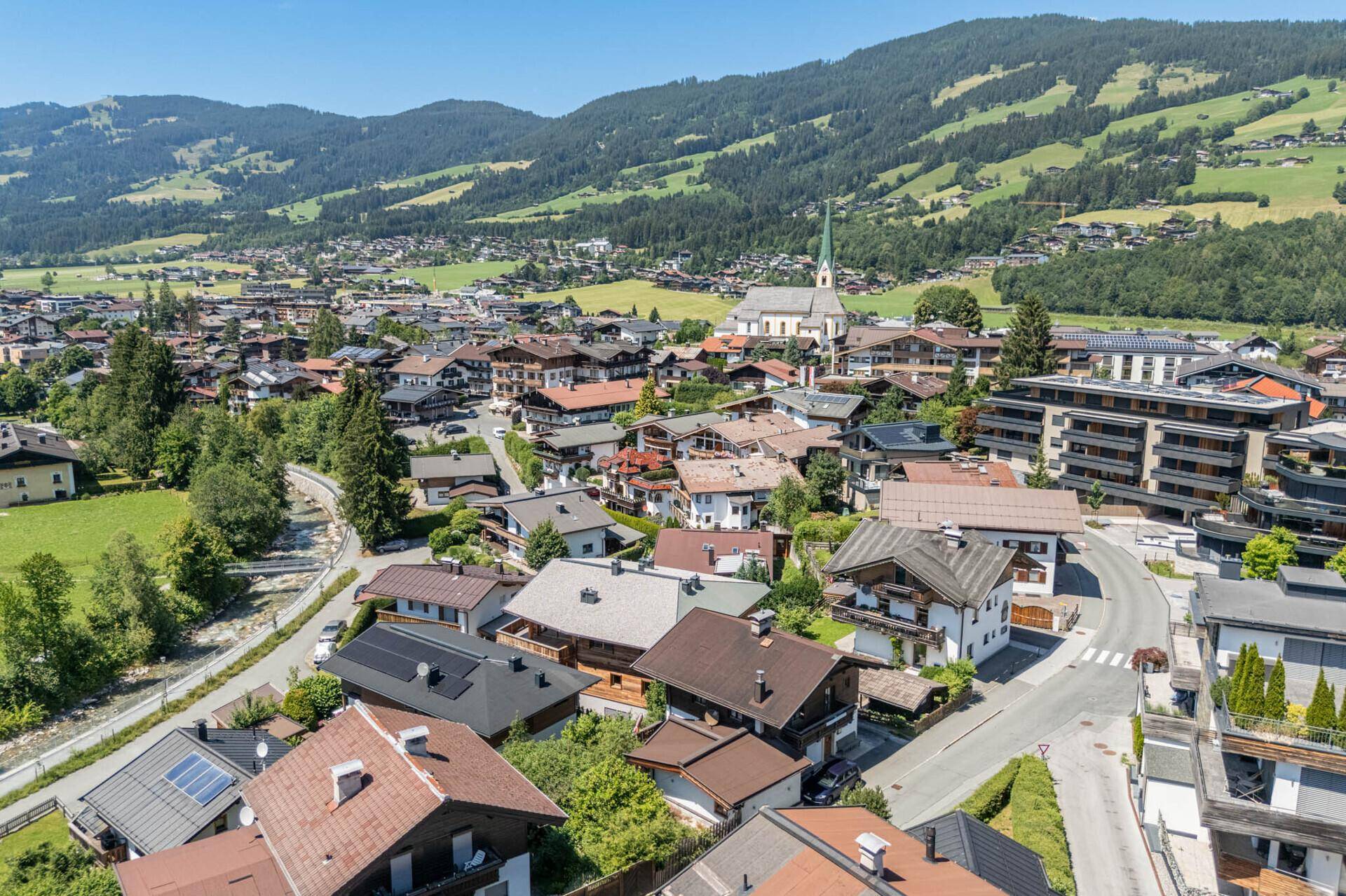 Panoramablick auf ein malerisches Dorf in den Alpen, umgeben von grünen Hügeln und Bergen.