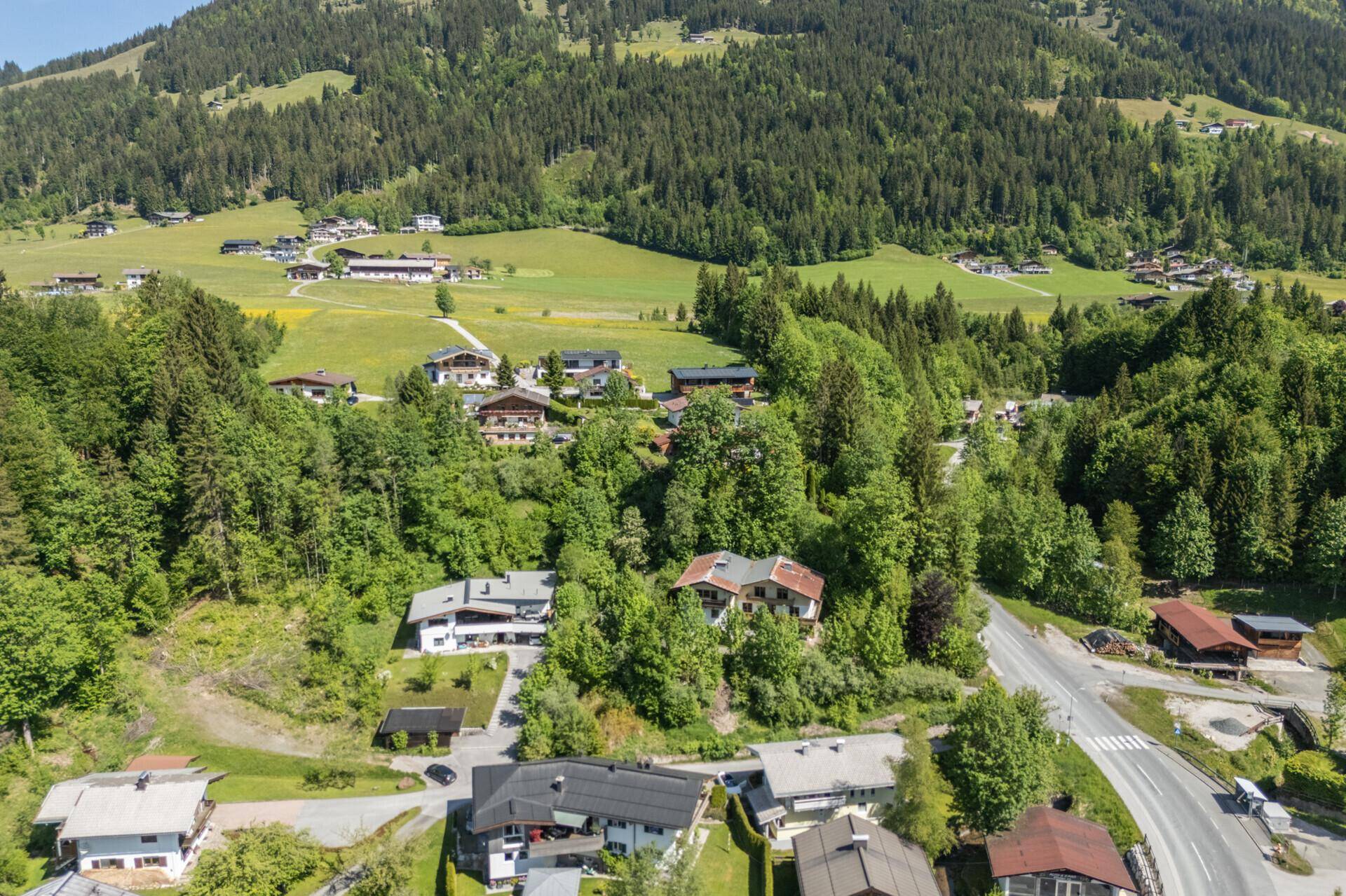 Weitläufige Luftaufnahme eines charmanten Bergdorfes, umgeben von üppiger Natur und bewaldeten Hängen.