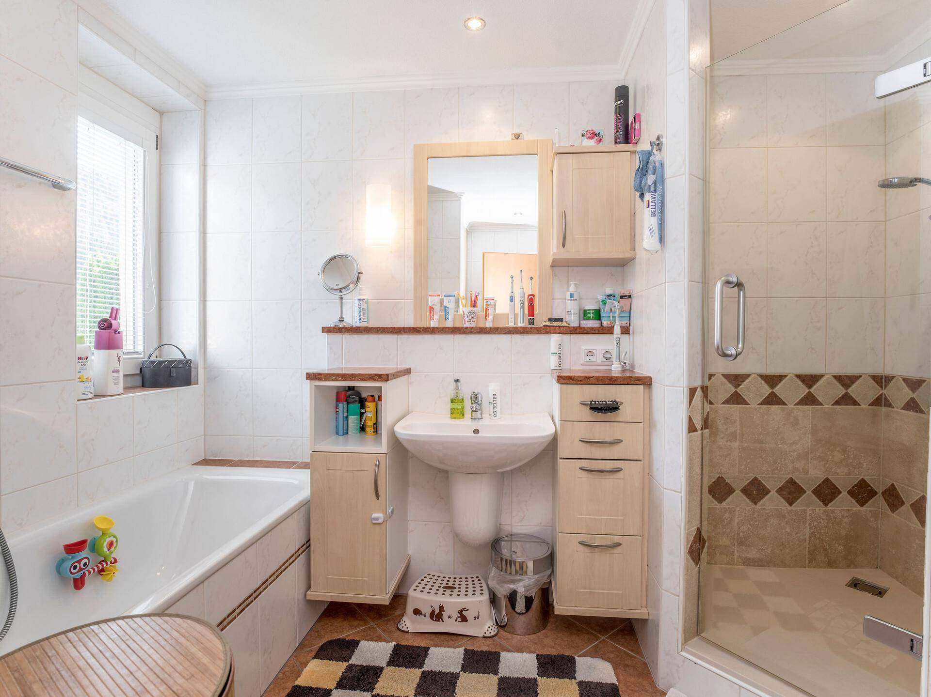 Helles Badezimmer mit Badewanne, Duschkabine, Einzelwaschbecken und beigen Fliesen.