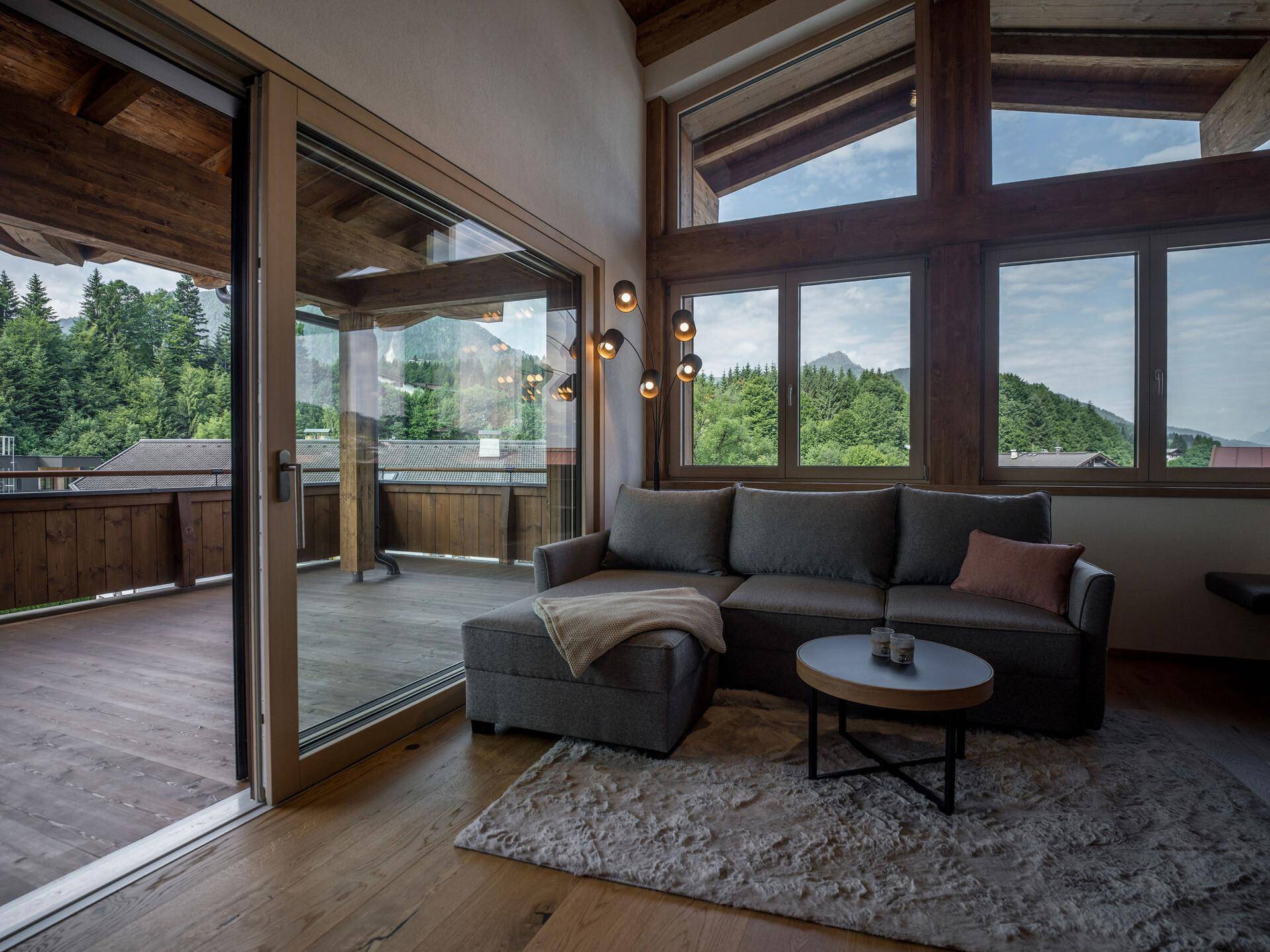 Helles Wohnzimmer mit gemütlichem Sofa und Zugang zu einer großen Holzterrasse mit Bergblick.