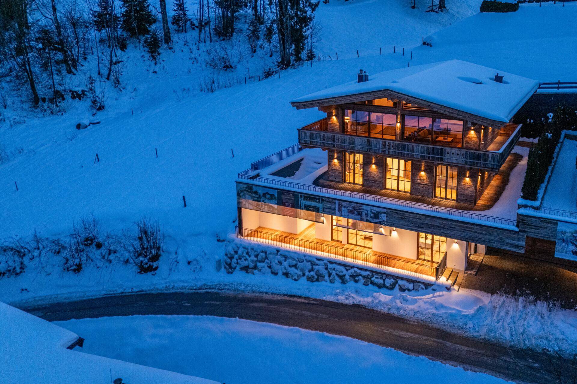 Modernes Chalet mit Holzfassade und großen Fensterfronten, eingebettet in eine verschneite Berglandschaft.