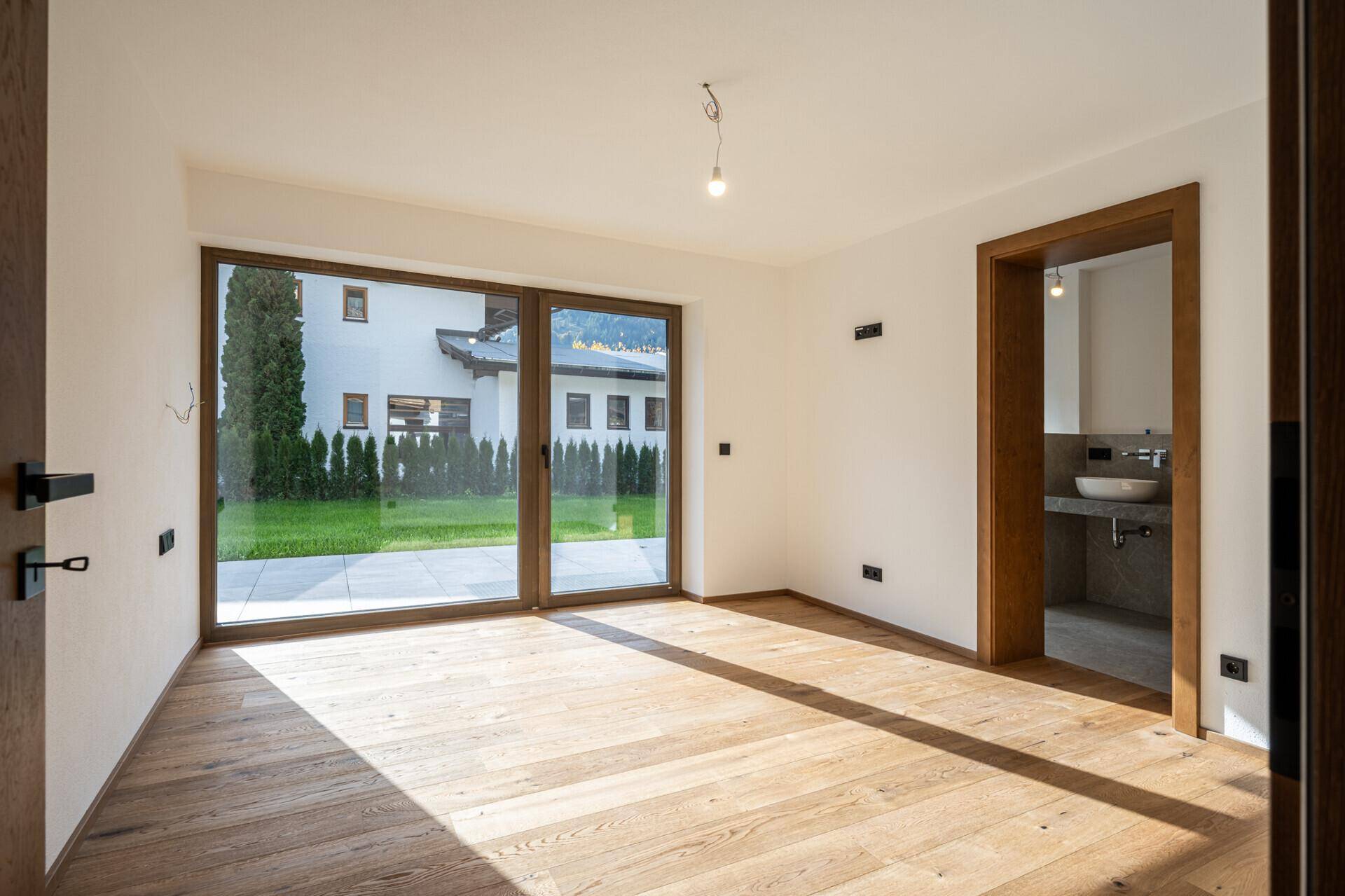Helles Schlafzimmer mit Holzboden, großen Fenstern und Zugang zum Garten.