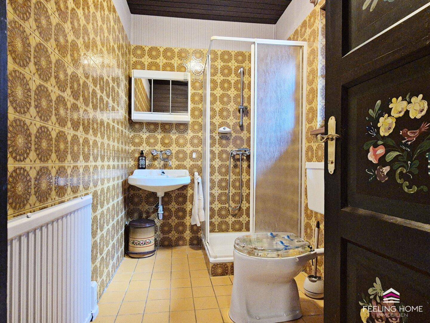 Badezimmer im charmanten 80er-Jahre-Stil mit gemusterten Fliesen, Dusche und Waschbecken.
