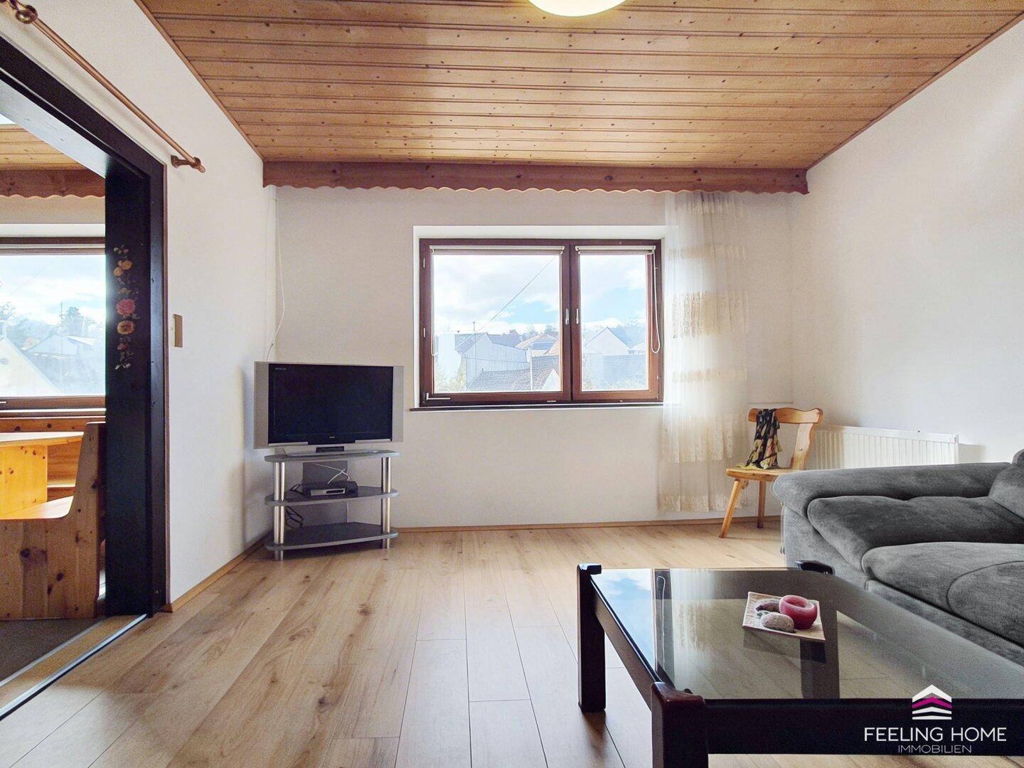 Gemütliches Wohnzimmer mit Holzbalkendecke, Parkettboden und einem Fenster mit Blick ins Grüne.