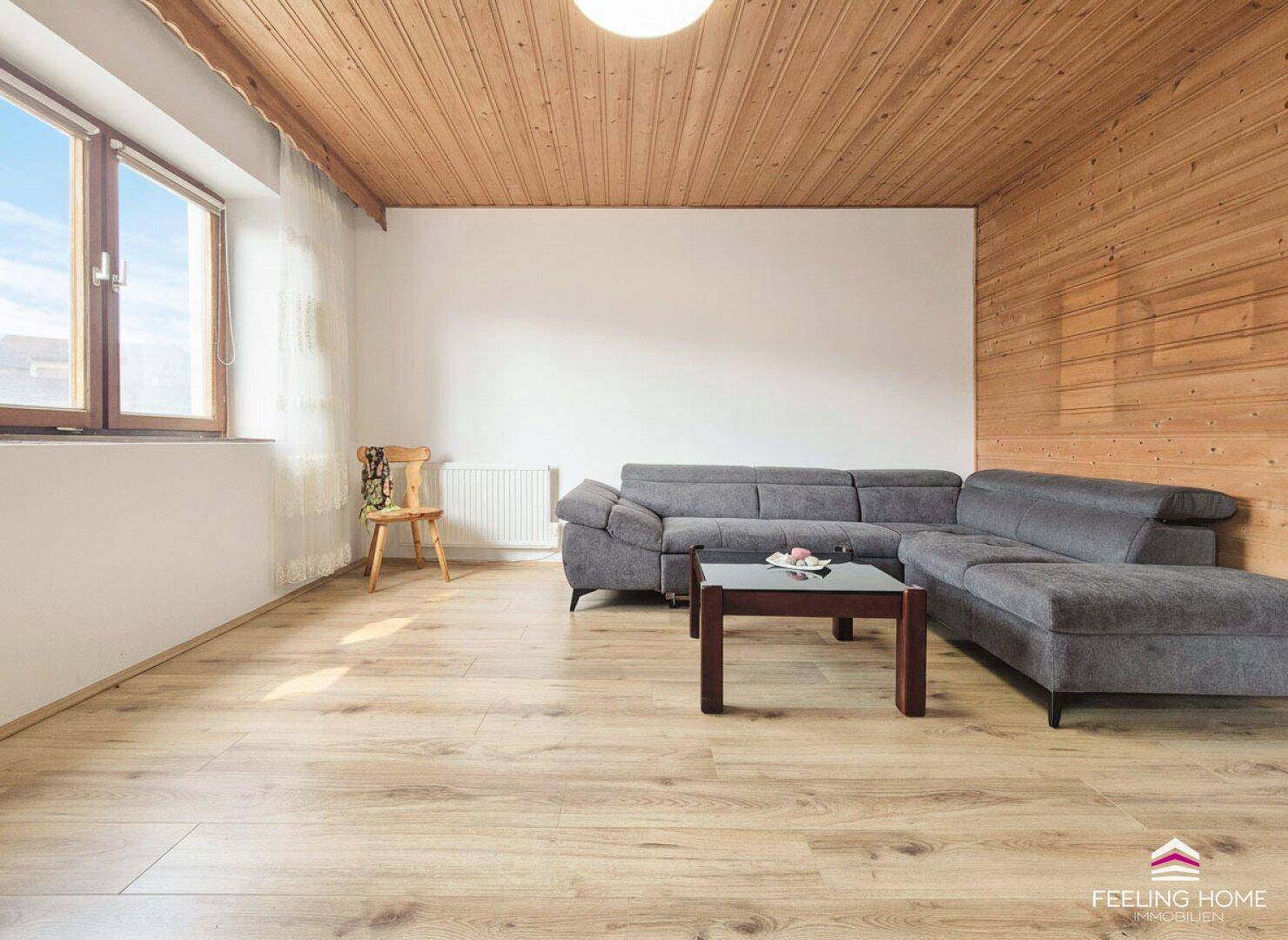 Helles Wohnzimmer mit Holzbalkendecke, Parkettboden und einer bequemen Eckcouch für entspannte Abende.