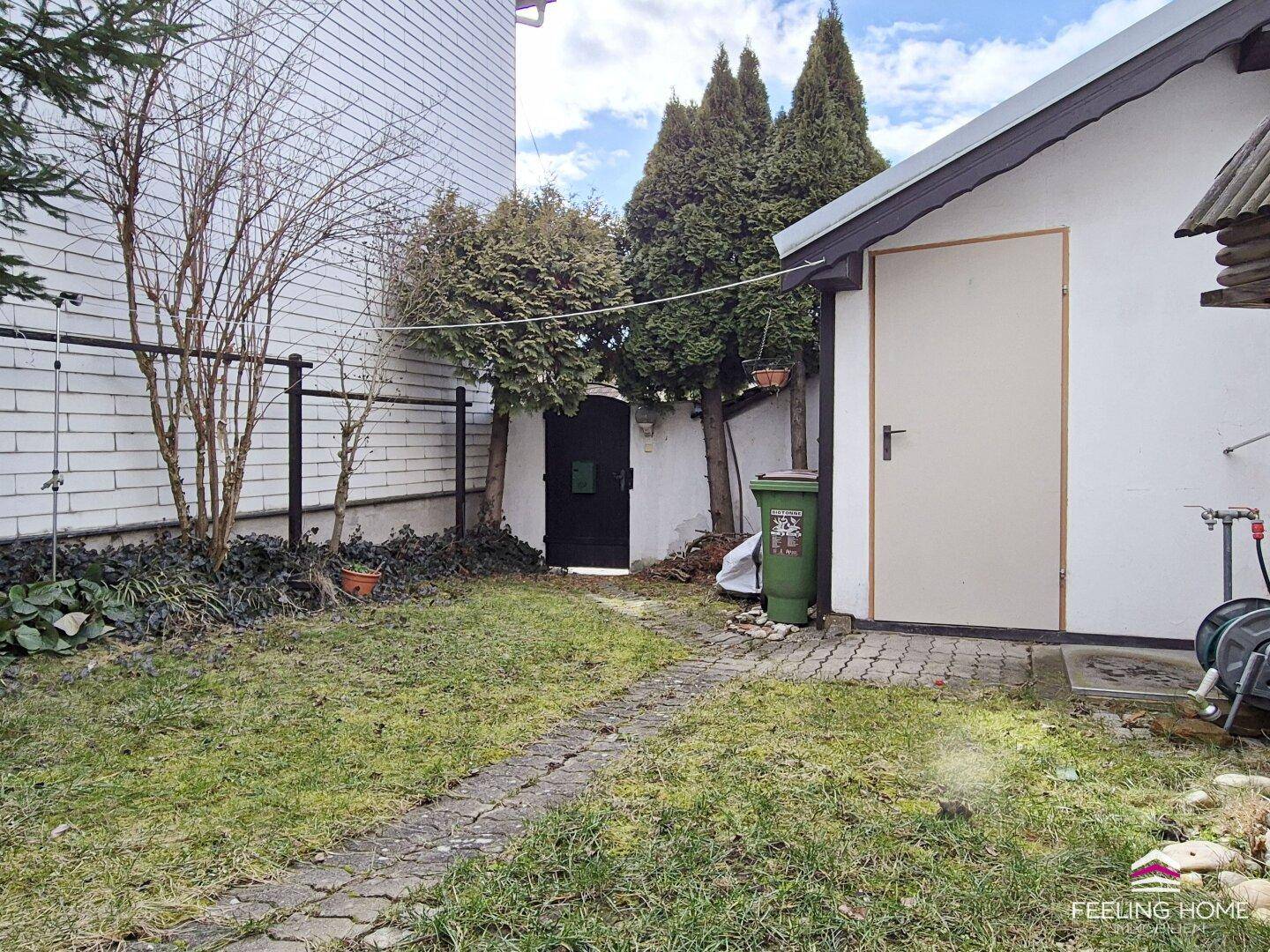 Gartenbereich mit Rasen, einem praktischen Gartenhaus und einem Zugang durch ein Holztor.