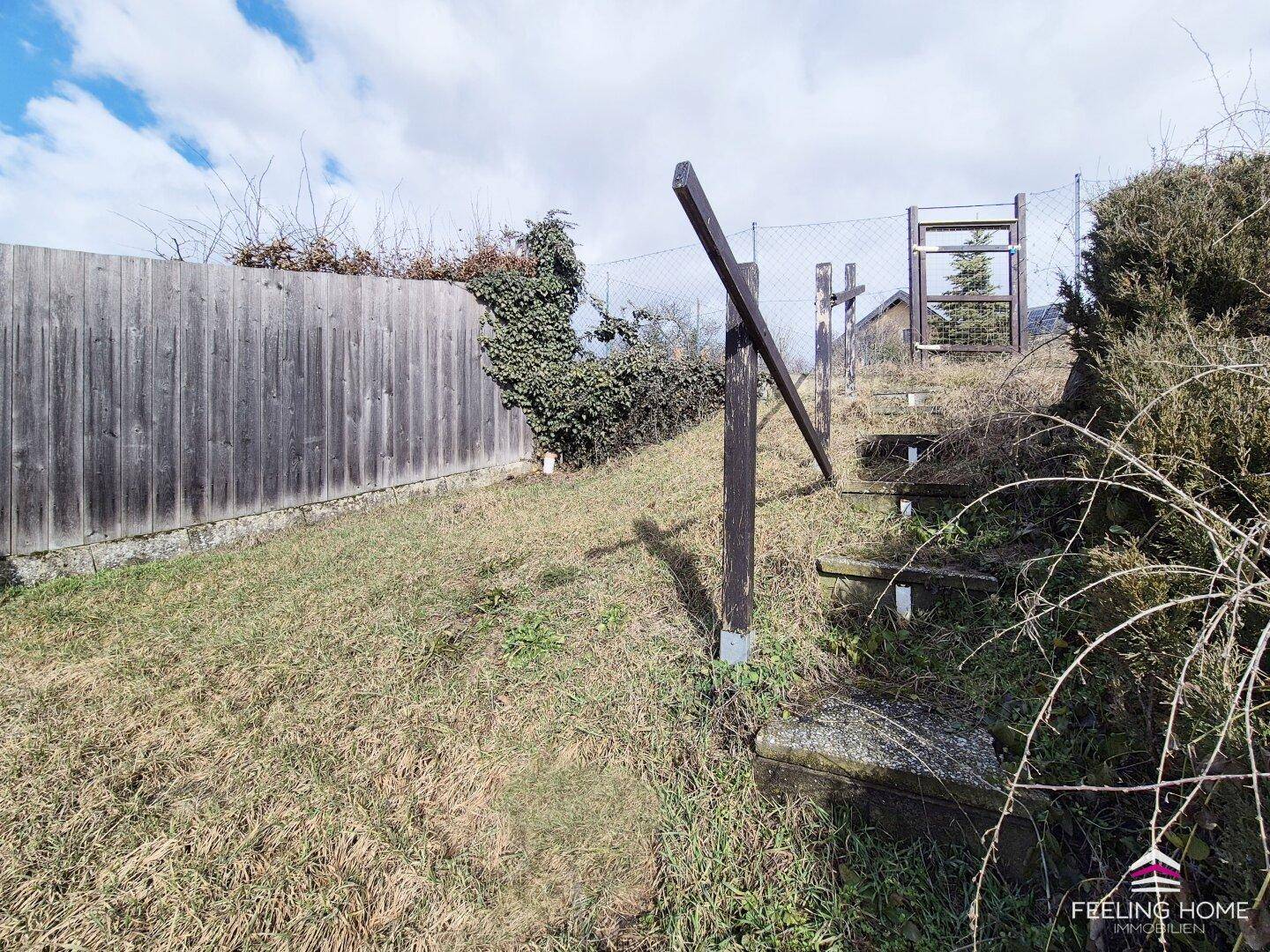 Hanglage im Garten mit einem Holzzaun, einer Treppe und einem schönen Blick in die Ferne.