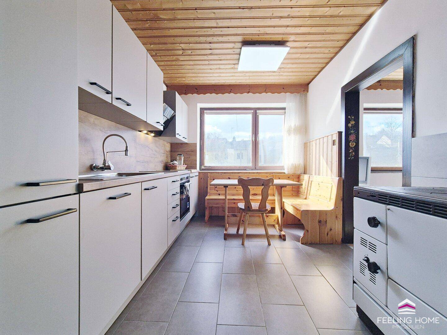 Helle Küche mit modernen weißen Schränken, Fliesenboden und einem gemütlichen Essbereich am Fenster.
