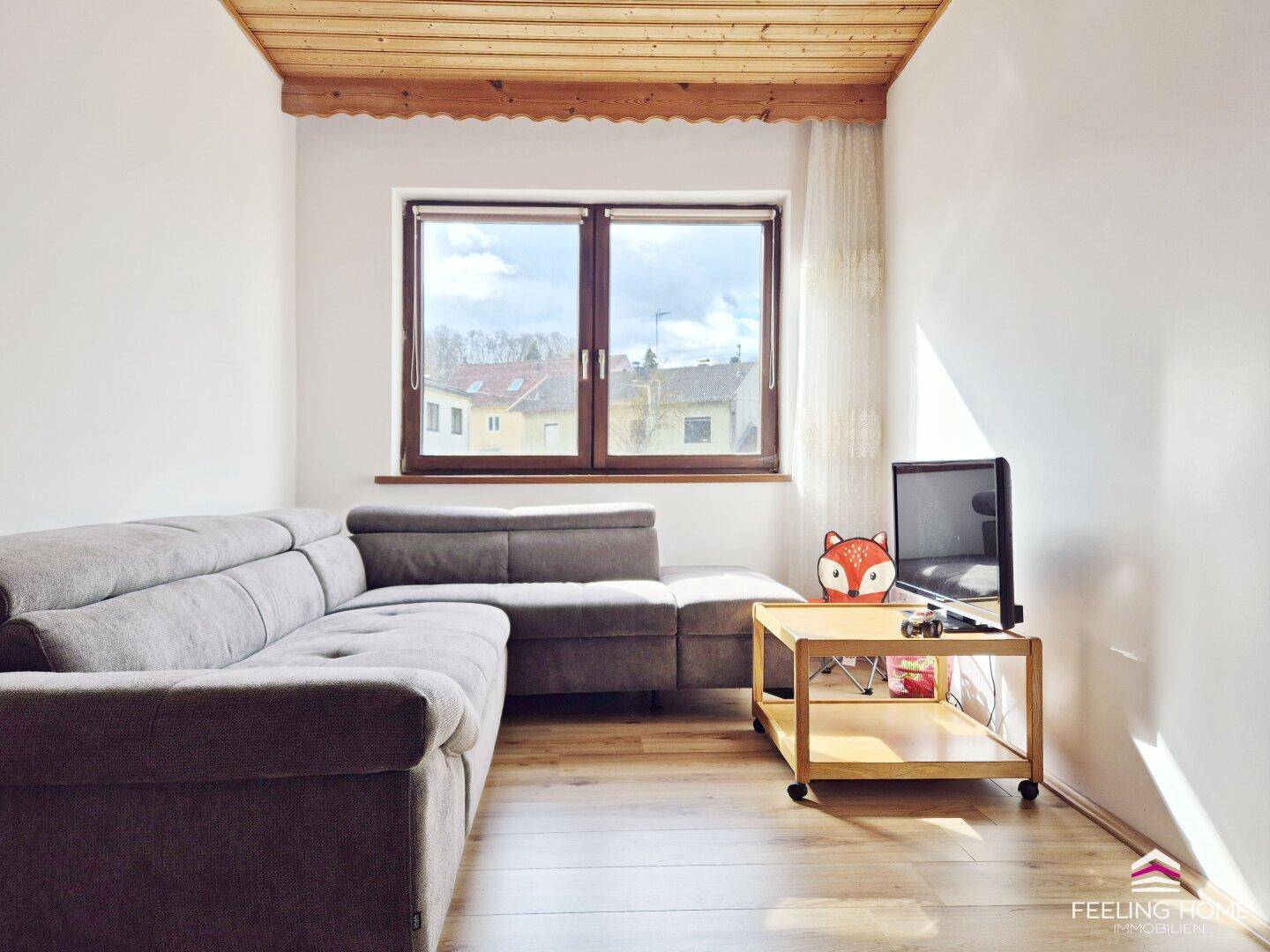 Kleines Wohnzimmer mit Holzbalkendecke, Parkettboden und einem großen Fenster für viel Tageslicht.