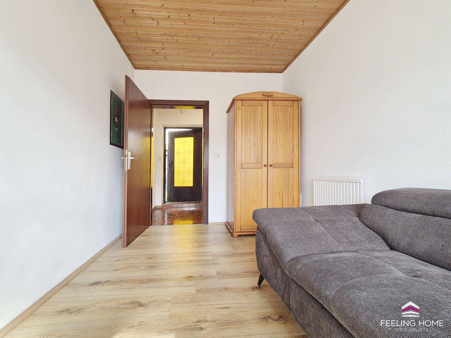 Wohnzimmer mit Holzbalkendecke, Parkettboden und einem offenen Zugang zum Flurbereich.