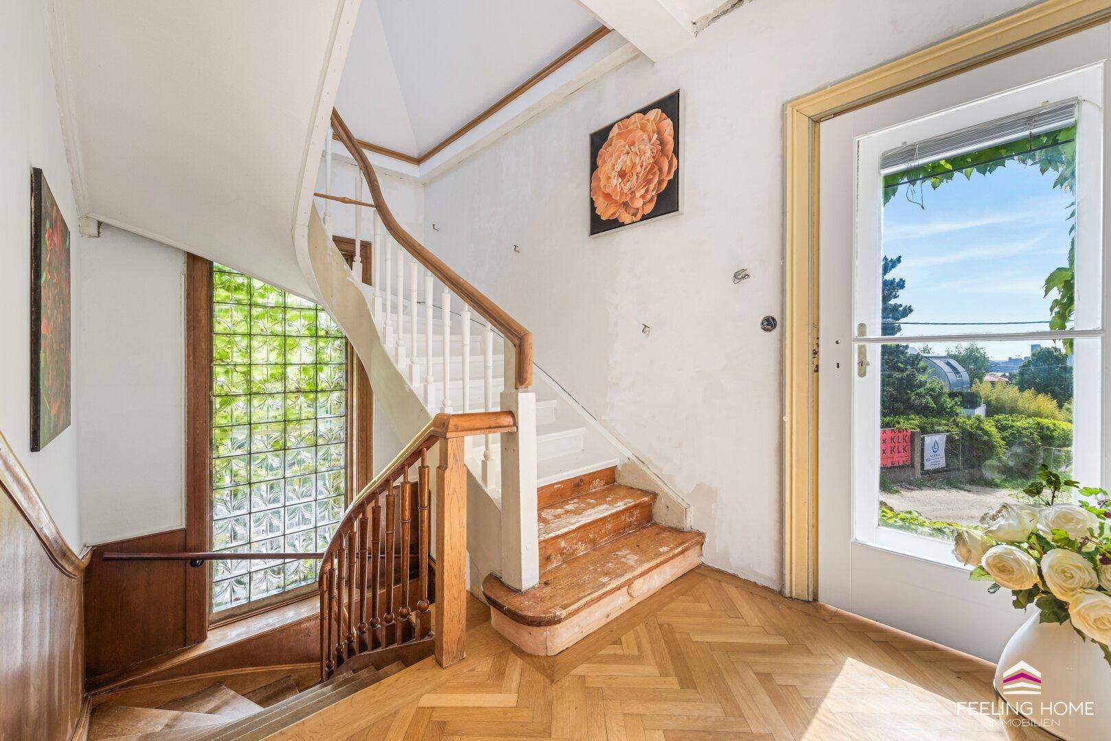 Heller Treppenaufgang mit Fischgrätparkett, Holzgeländer und einem großen Fenster.