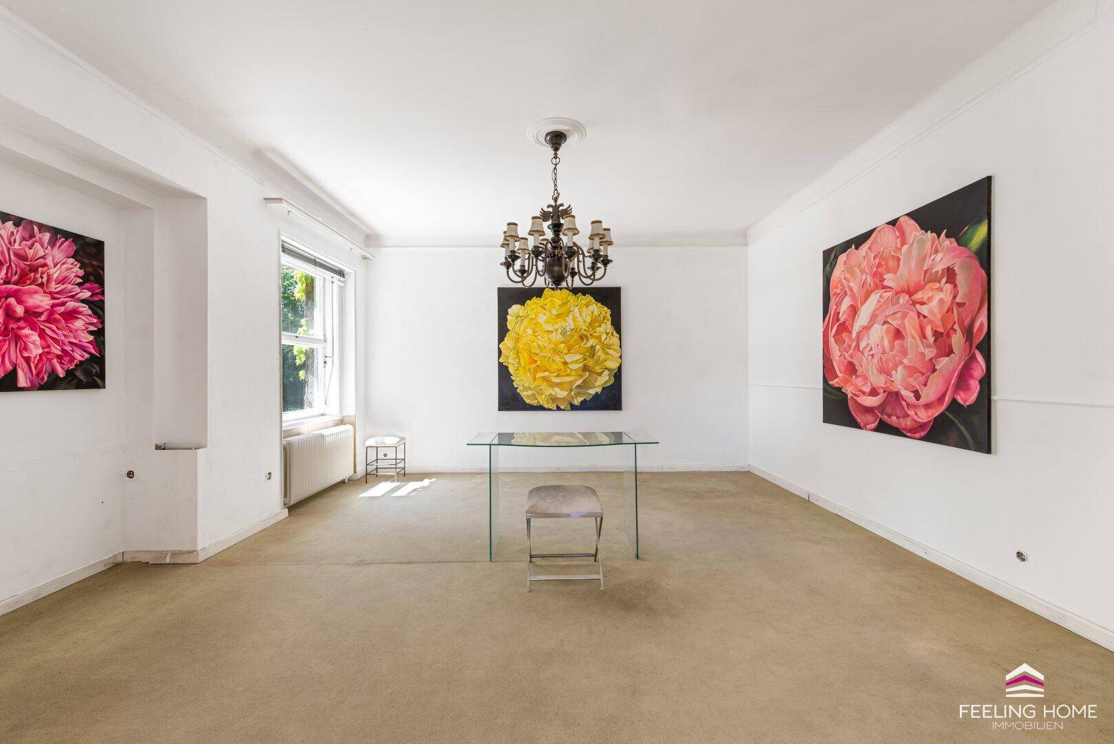 Heller Wohnbereich mit Teppichboden, Kunstwerken an den Wänden und einem modernen Glastisch.
