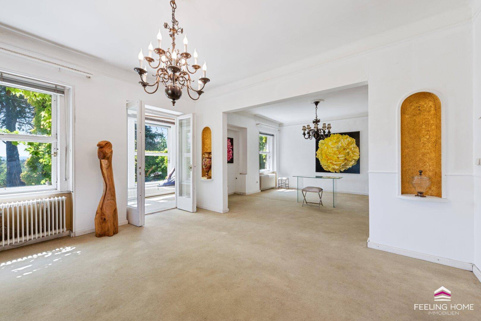 Geräumiges Wohnzimmer mit Teppichboden, hohen Decken und zwei eleganten Kronleuchtern.