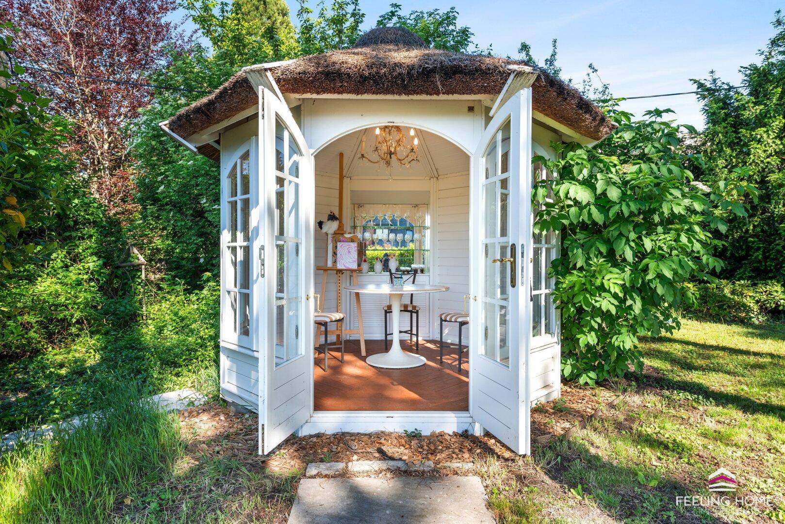 Charmantes Gartenhaus mit Reetdach und geöffneten Türen, ideal für gemütliche Stunden im Grünen.