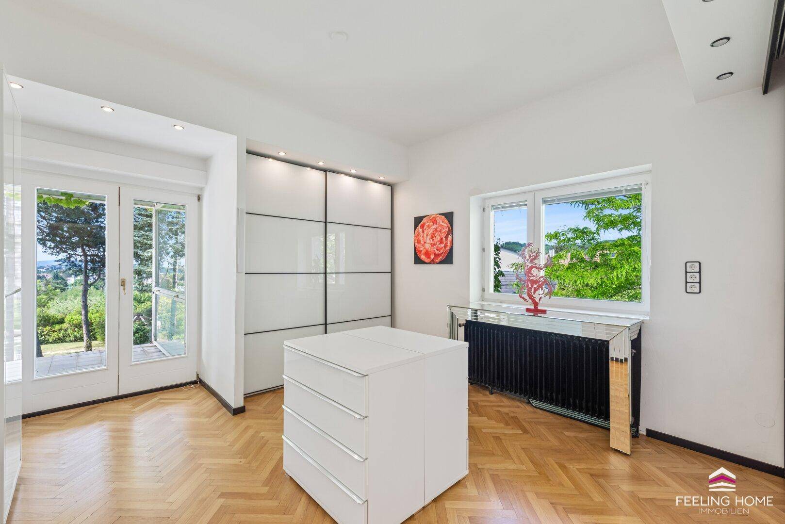 Helles Schlafzimmer mit Fischgrätparkett, Einbauschränken und Zugang zum Balkon.