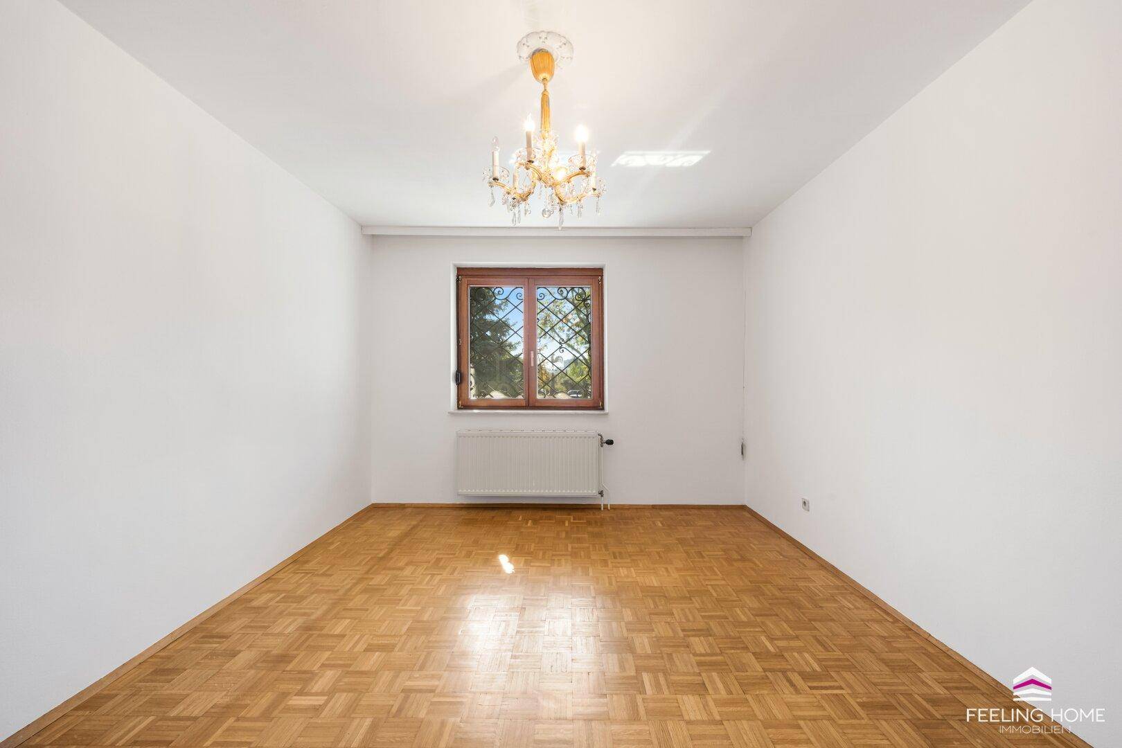 Schlafzimmer mit Parkettboden, weiß gestrichenen Wänden und einem Fenster mit Gitter.