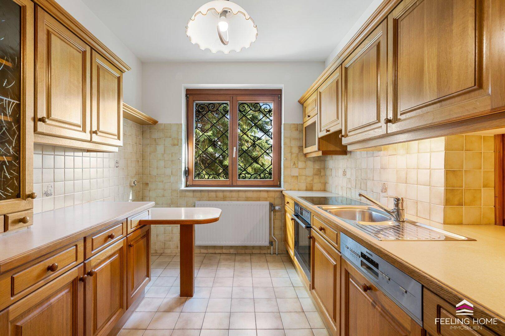 Traditionelle Holzküche mit Einbauschränken, Fliesenboden und Fenster mit Gitter.