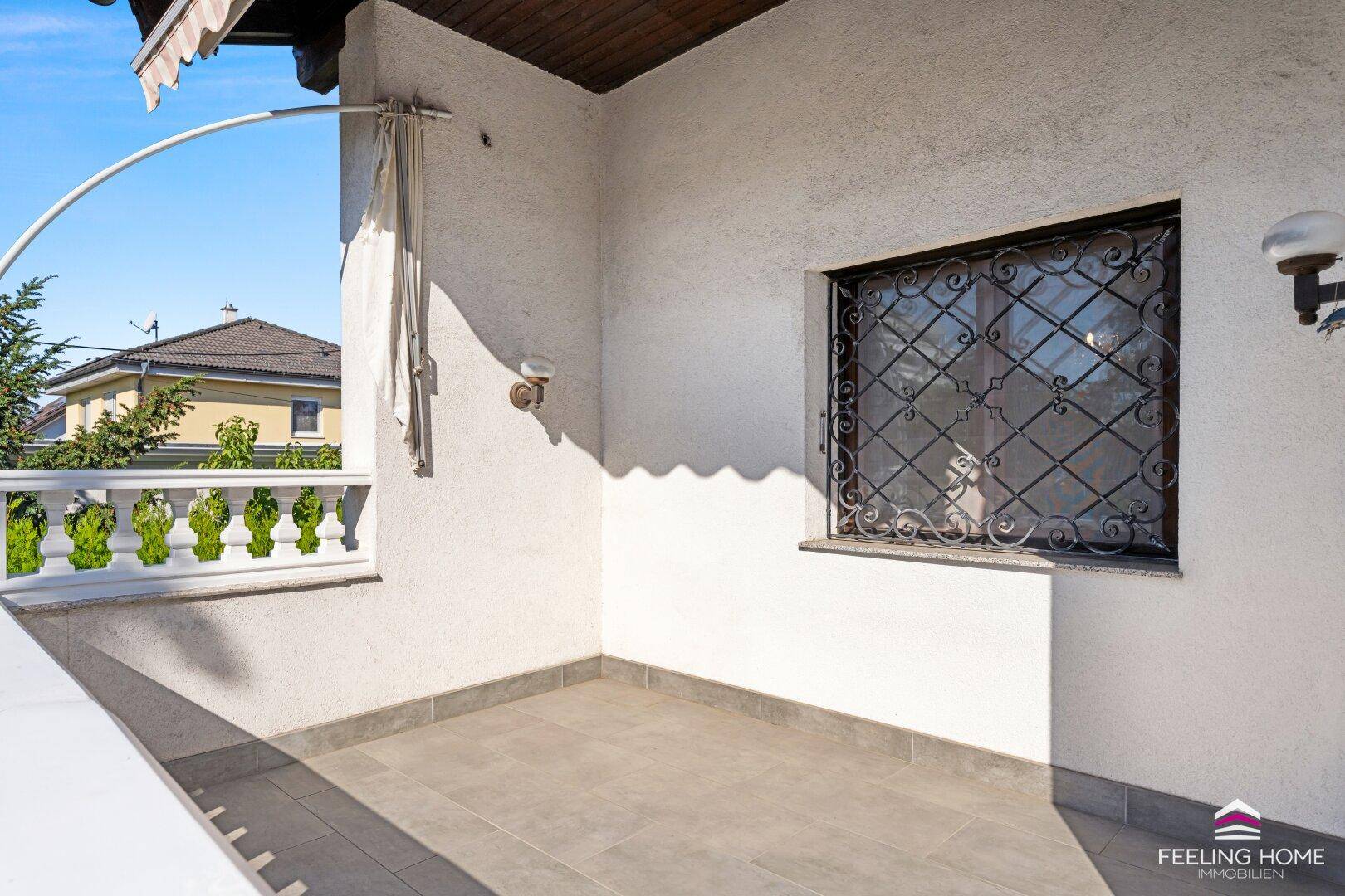 Kleiner, gefliester Balkon mit schmiedeeisernem Fenstergitter und weißer Fassade des Hauses.