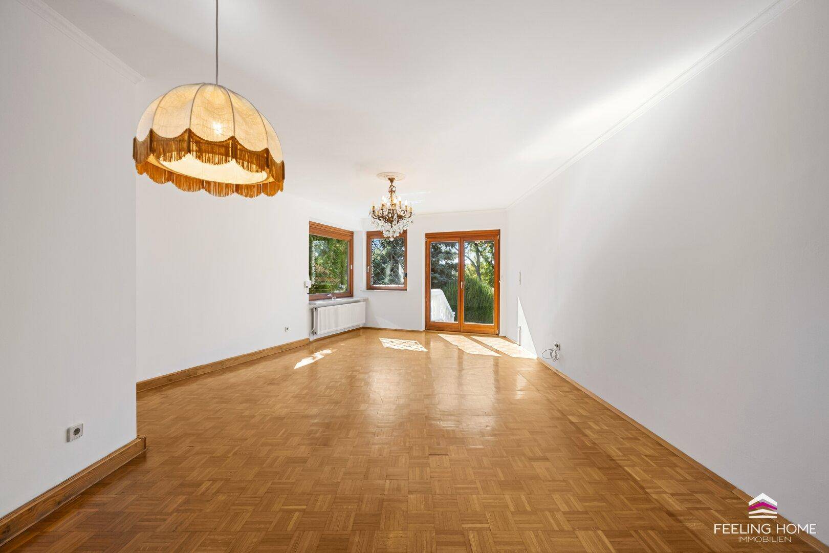Geräumiges Wohnzimmer mit Fischgrätparkett und viel Tageslicht durch mehrere Fenster.