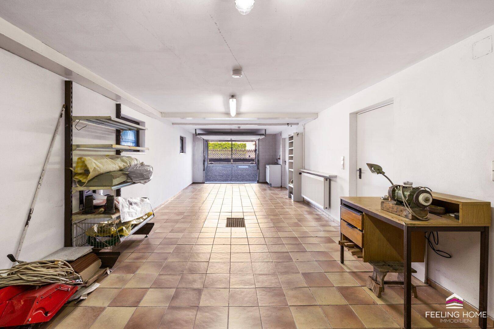 Geräumige Garage mit Fliesenboden, Regalen und direktem Zugang nach draußen.