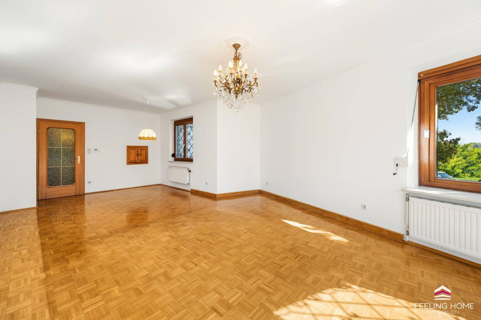 Wohnzimmer mit klassischem Parkettboden, weiß gestrichenen Wänden und einer Holztür.