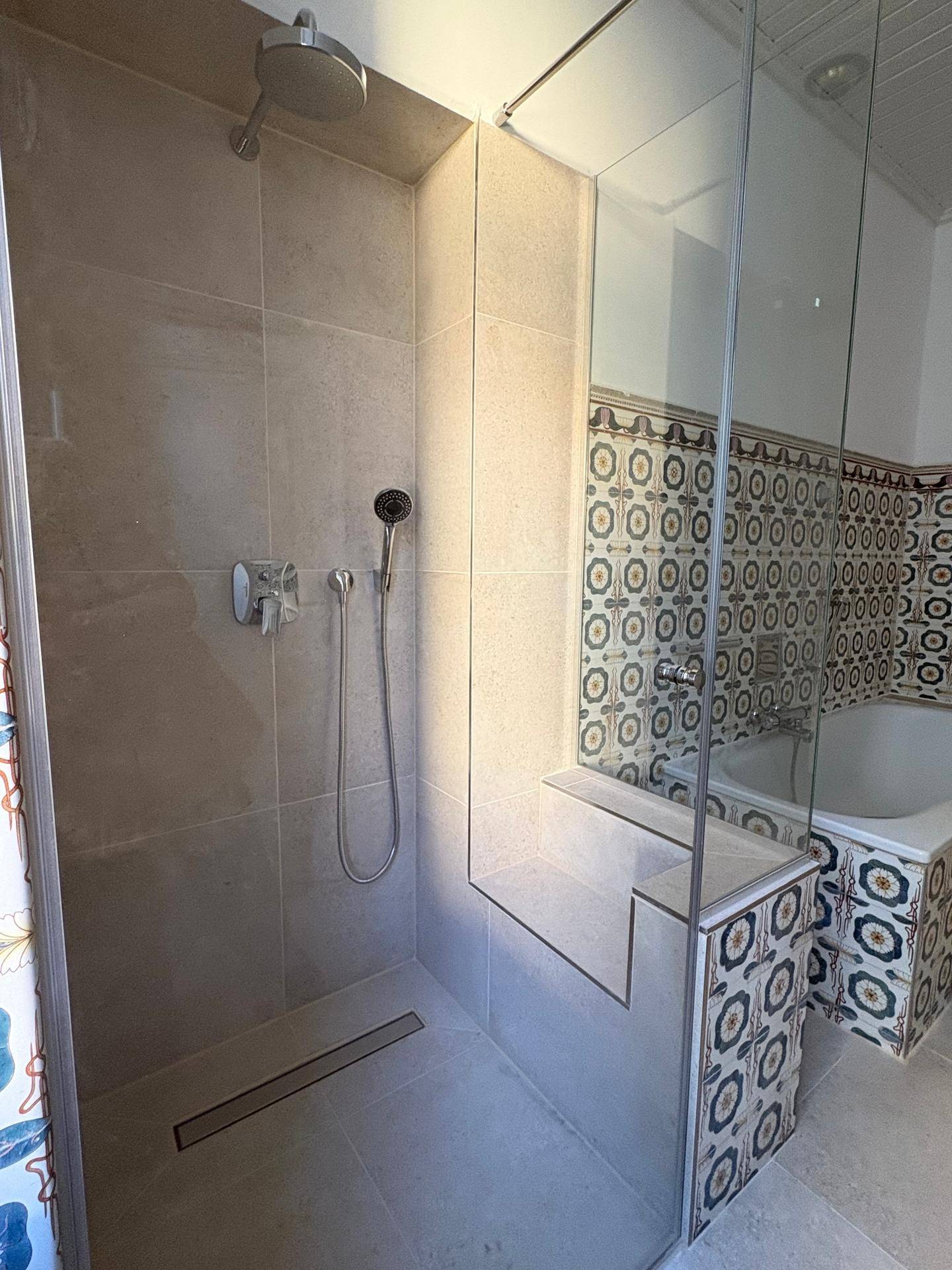 Detailansicht der modernen, begehbaren Dusche mit Regenduschkopf und integrierter Sitzbank im Badezimmer.