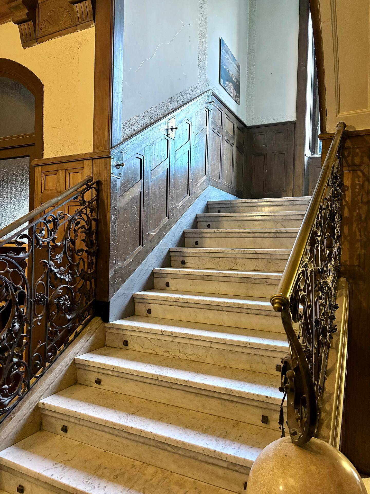 Prunkvolles Treppenhaus mit Marmorstufen, Holzvertäfelung und kunstvollem schmiedeeisernem Geländer.