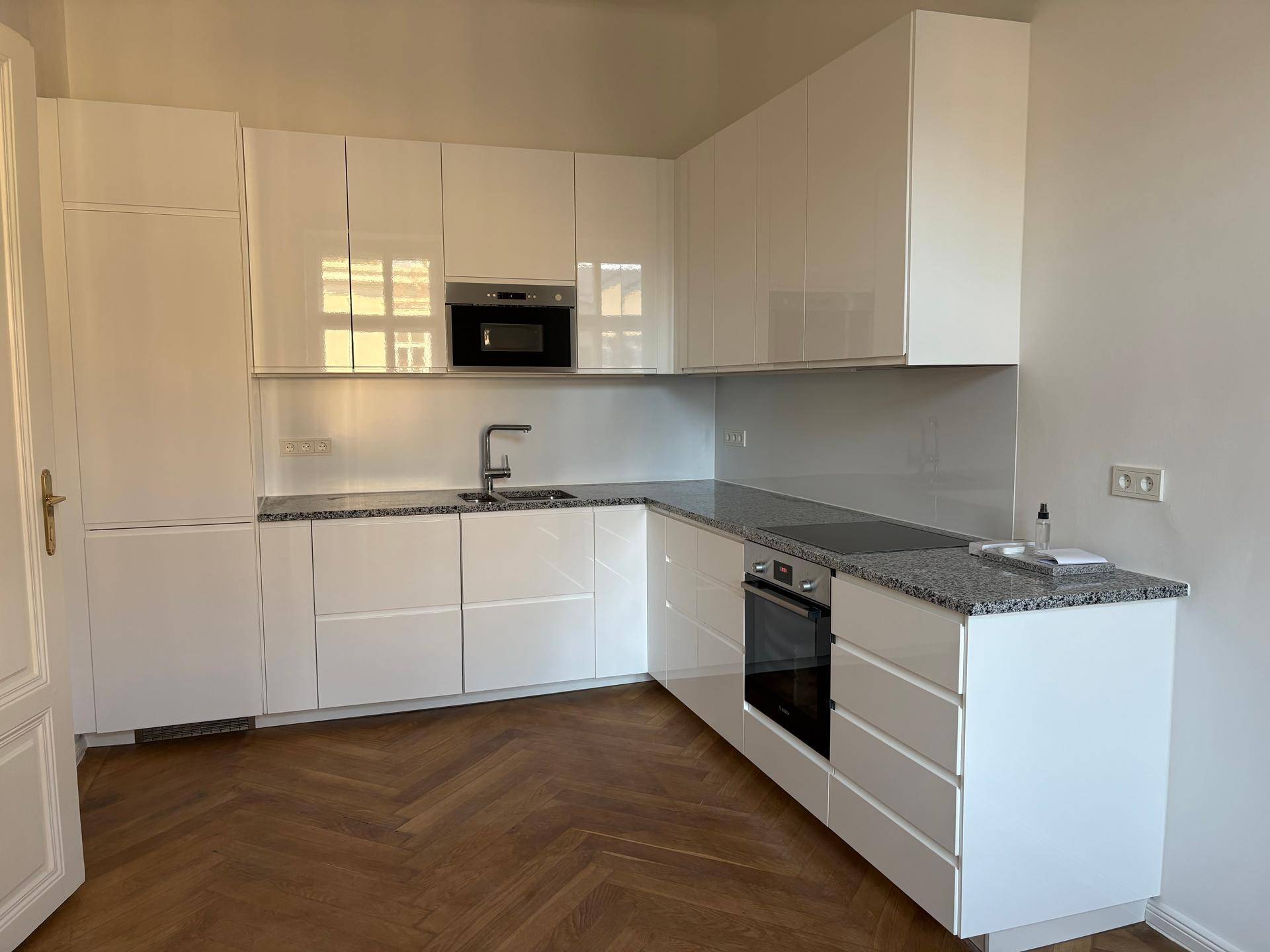 Moderne Einbauküche mit weißen Hochglanzfronten, Granitarbeitsplatte und integrierten Geräten.