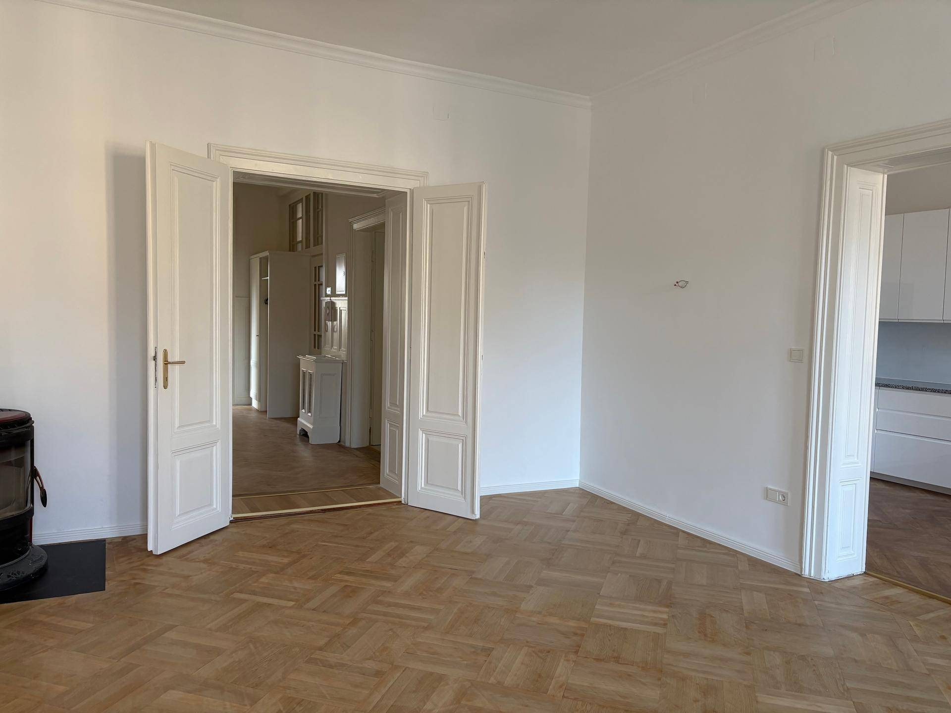 Helles Zimmer mit Fischgrätparkett und Flügeltüren, die den Zugang zu angrenzenden Bereichen ermöglichen.