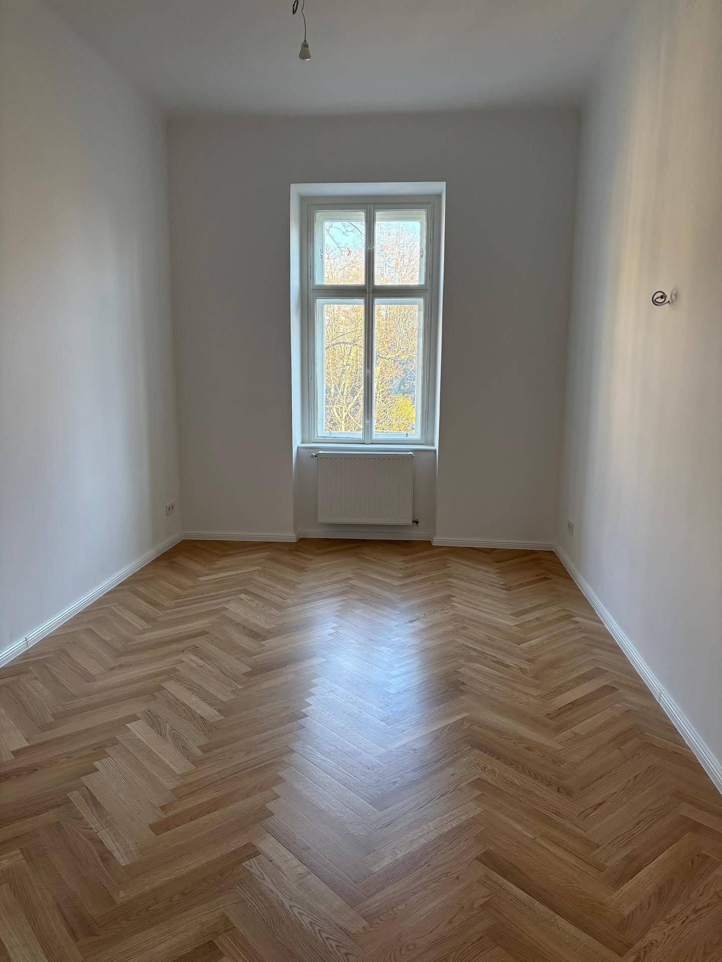 Ruhiges Zimmer mit Fischgrätparkettboden und einem großen Fenster, das den Raum erhellt.