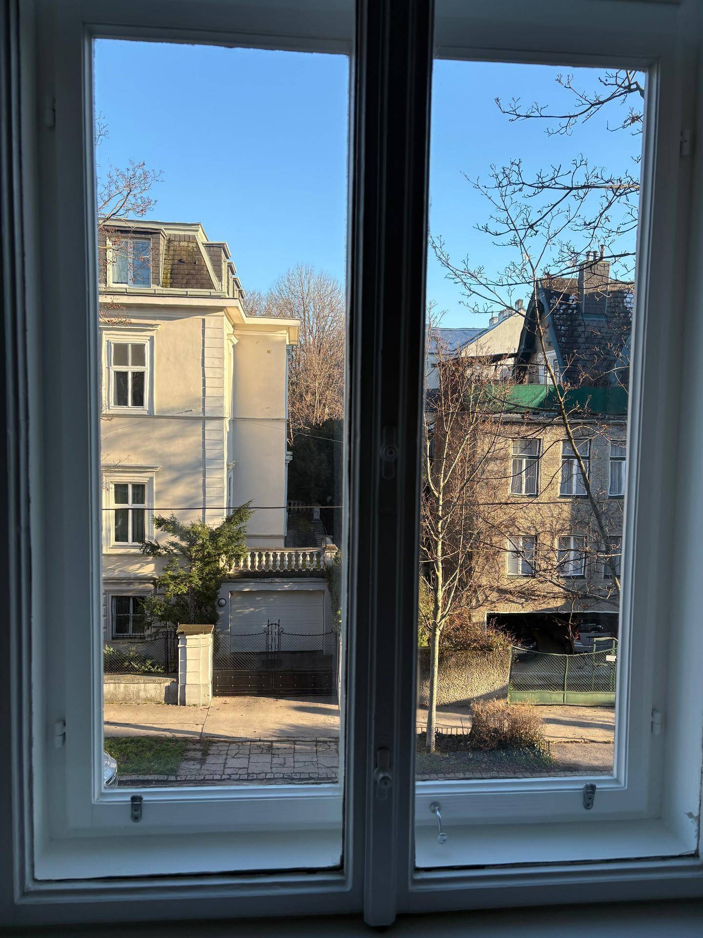 Ausblick aus dem Fenster auf die umliegenden Gebäude und Bäume in der sonnigen Nachbarschaft.