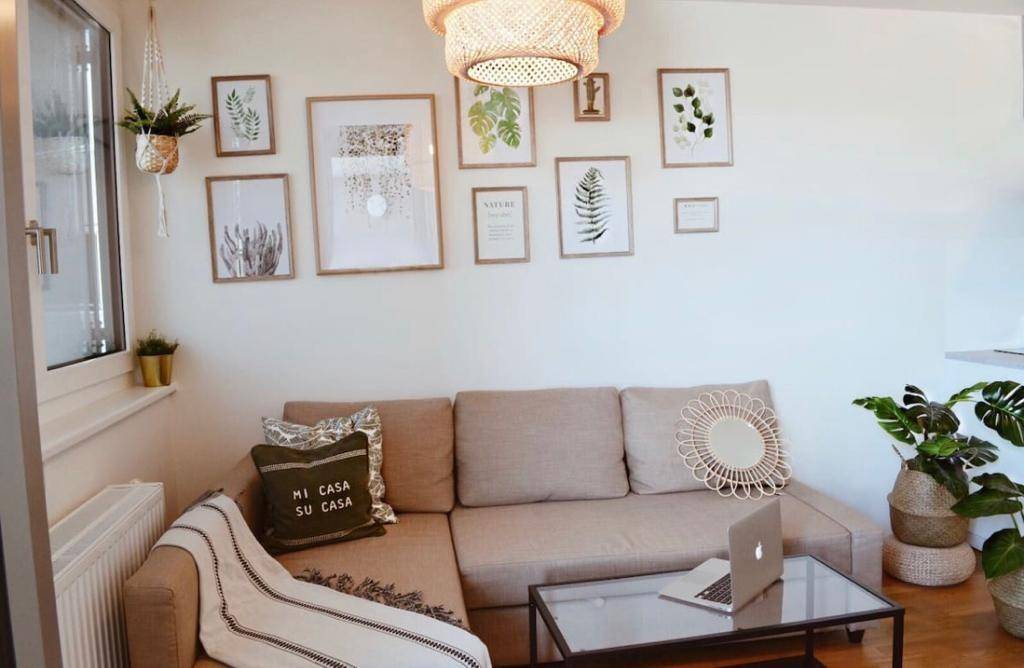 Gemütliches Wohnzimmer mit beigem Ecksofa, Couchtisch und Pflanzen, dekoriert mit Wandbildern.