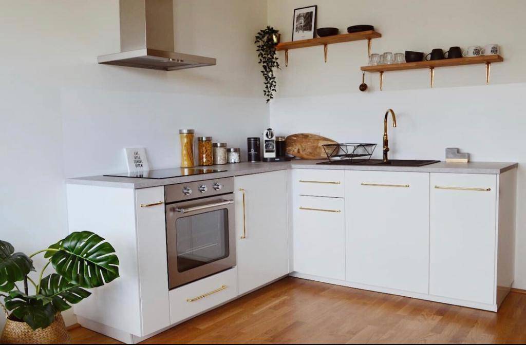 Moderne Küche mit weißen Schränken, Holzböden und Edelstahlgeräten, ausgestattet mit einem Backofen.
