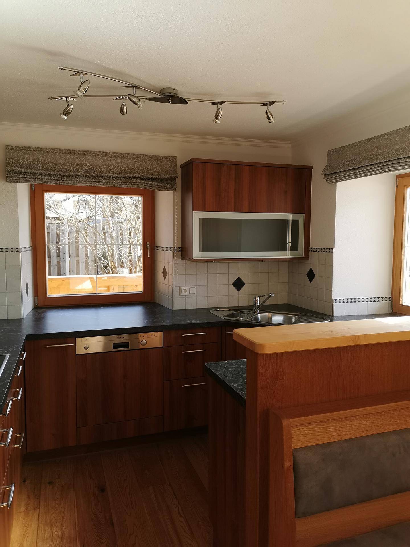 Holzküche mit dunkler Arbeitsplatte, Spüle und Fenster, die viel Licht hereinlässt.