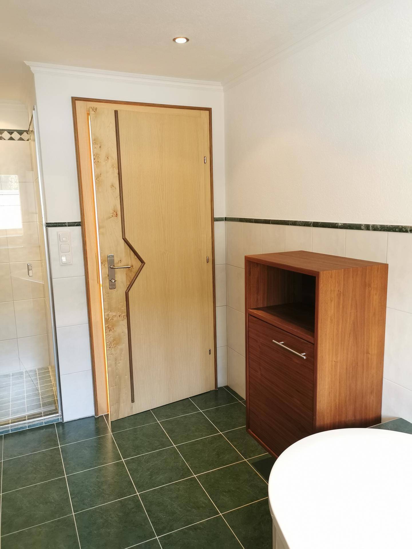 Badezimmertür aus Holz und gefliester Boden mit dunklen, grünen Fliesen.