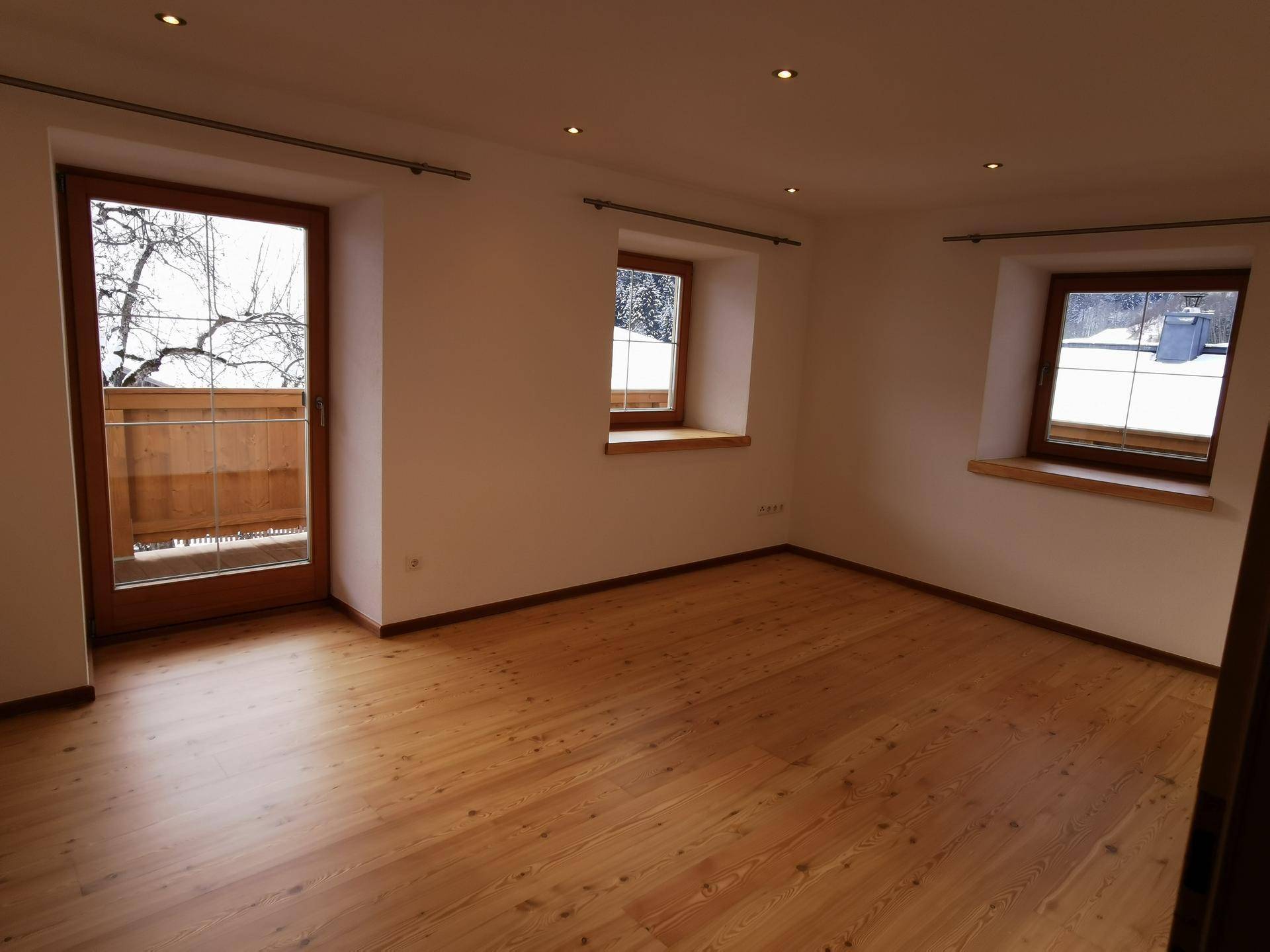 Heller Raum mit Holzboden und Zugang zu einem Balkon, der viel Tageslicht bietet.