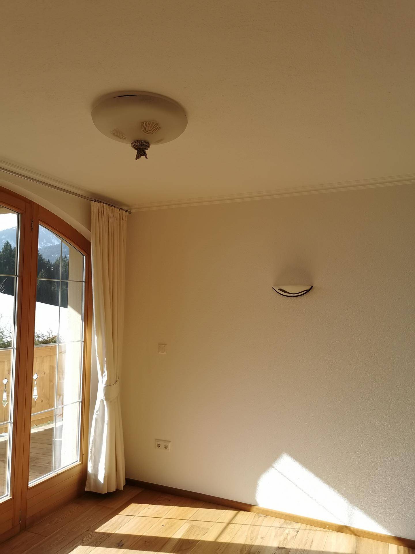 Deckenleuchte in einem hellen Raum mit Holztür und Vorhängen, die Tageslicht hereinlassen.