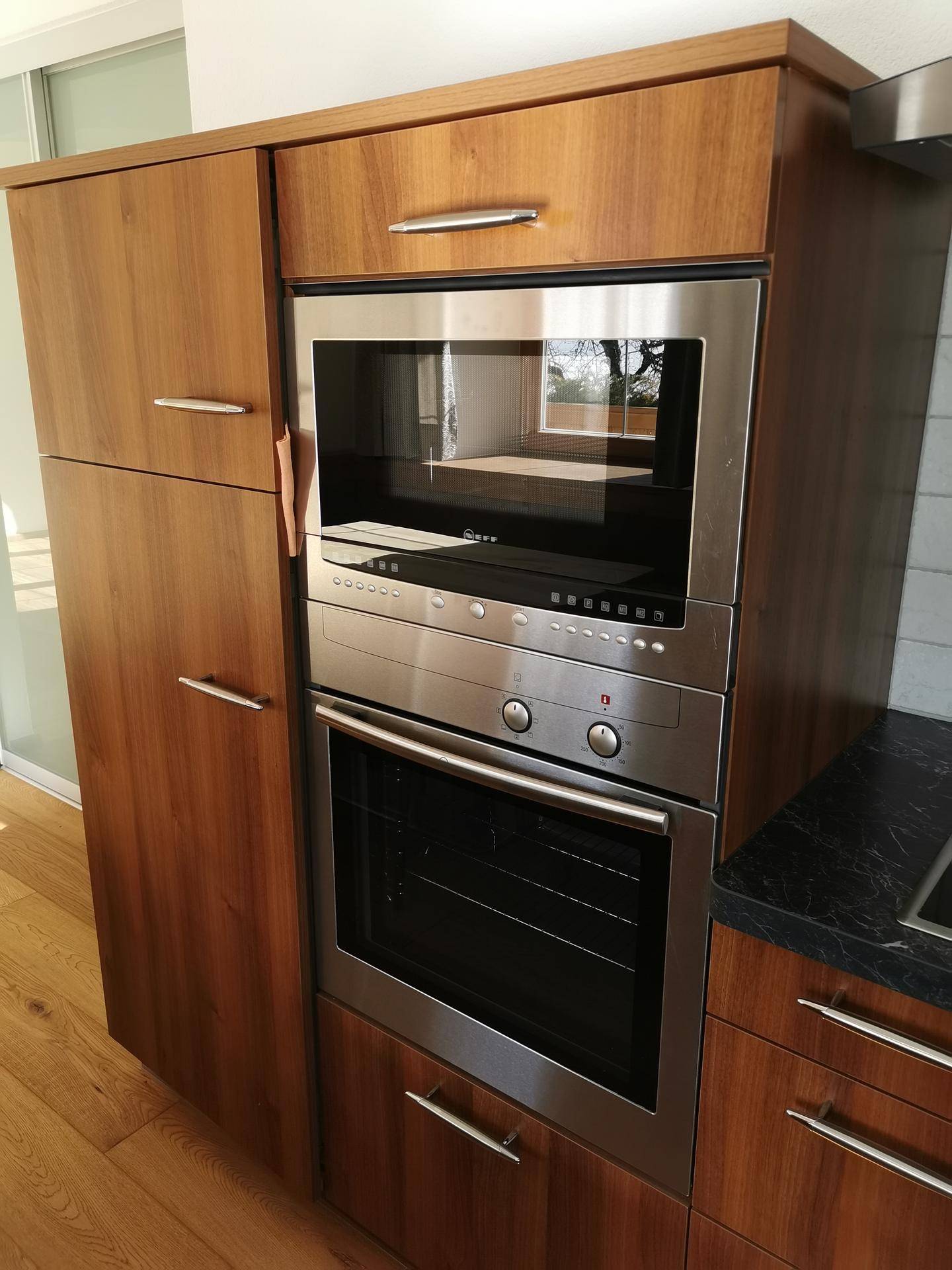 Integrierter Backofen und Mikrowelle aus Edelstahl in einem Holzschrank der Küche.