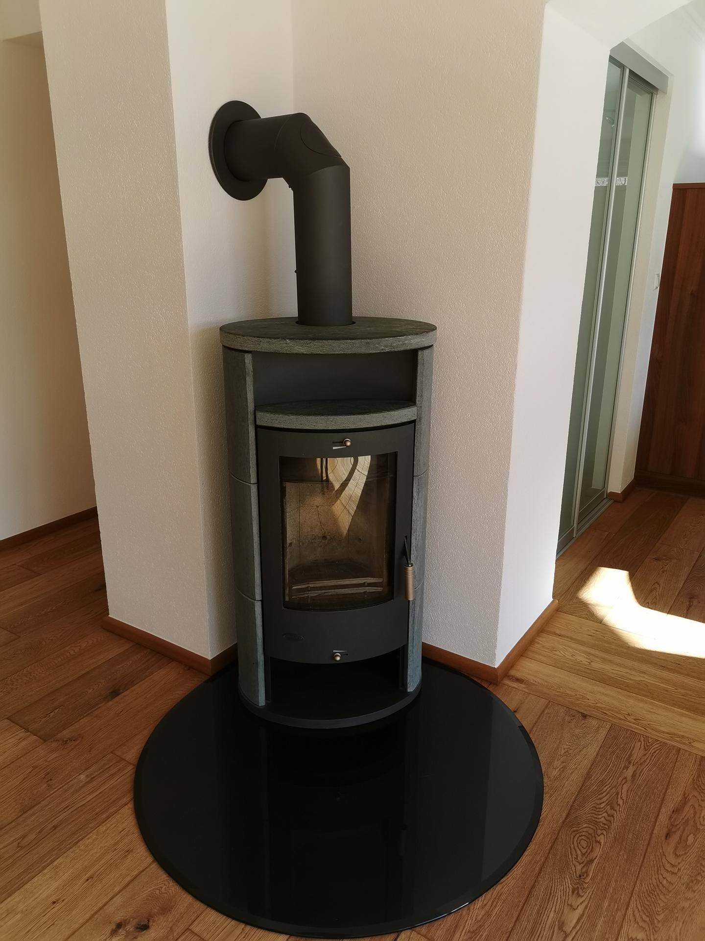 Moderner Holzofen mit schwarzer Bodenplatte in einer Ecke des Wohnbereichs.