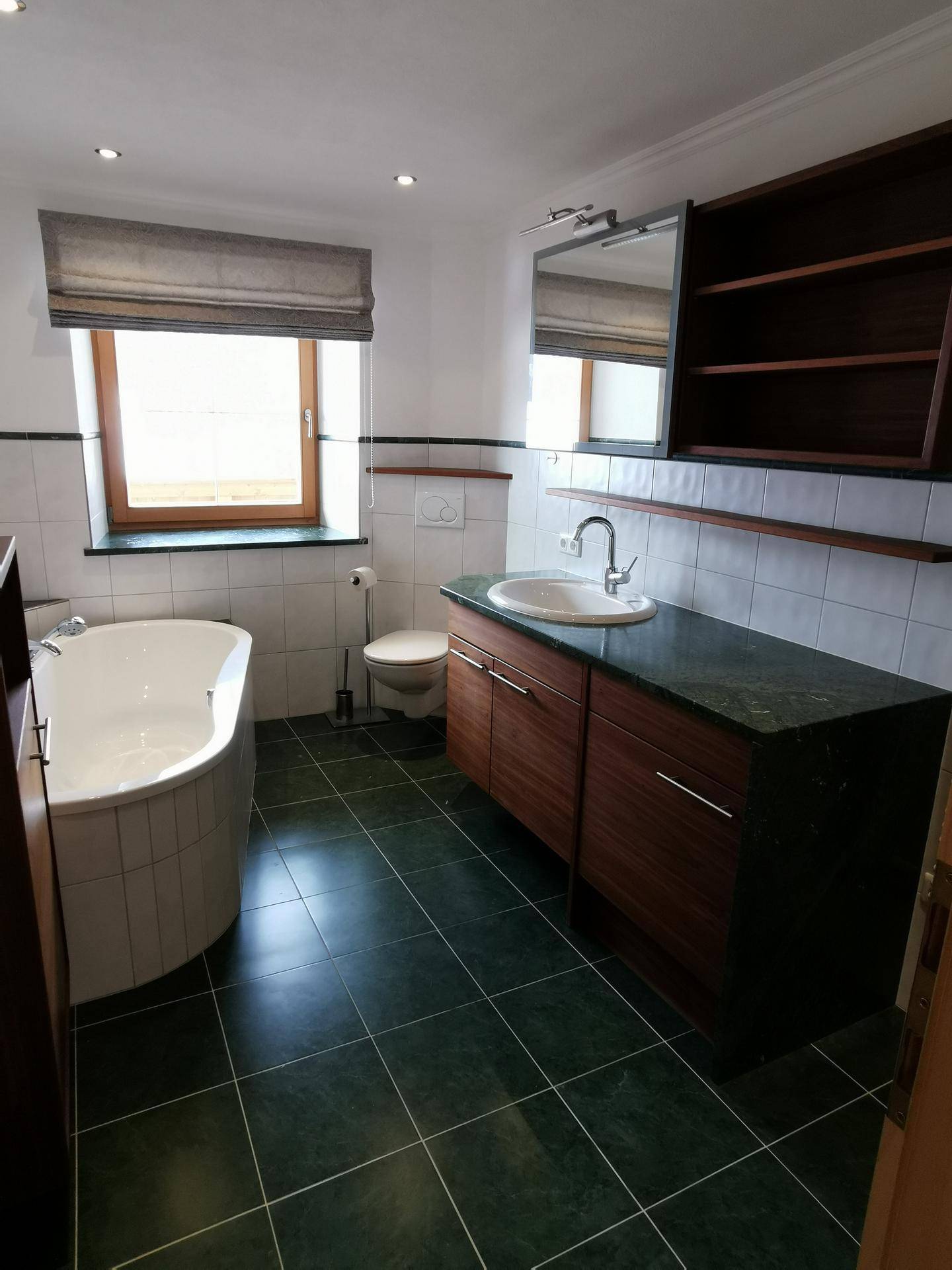 Badezimmer mit Badewanne, Waschtisch, Toilette und Fenster, alles in gutem Zustand.