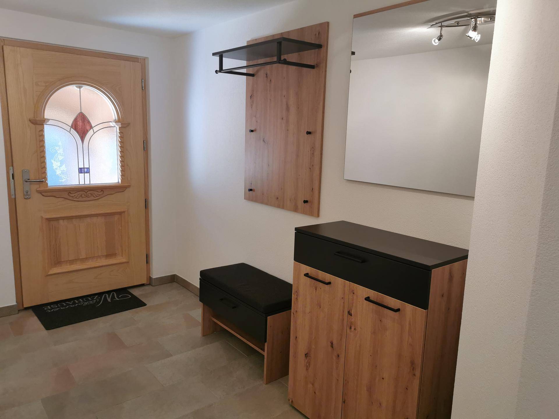 Eingangsbereich mit Holztür, Garderobe und Schuhschrank, alles in modernem Design.
