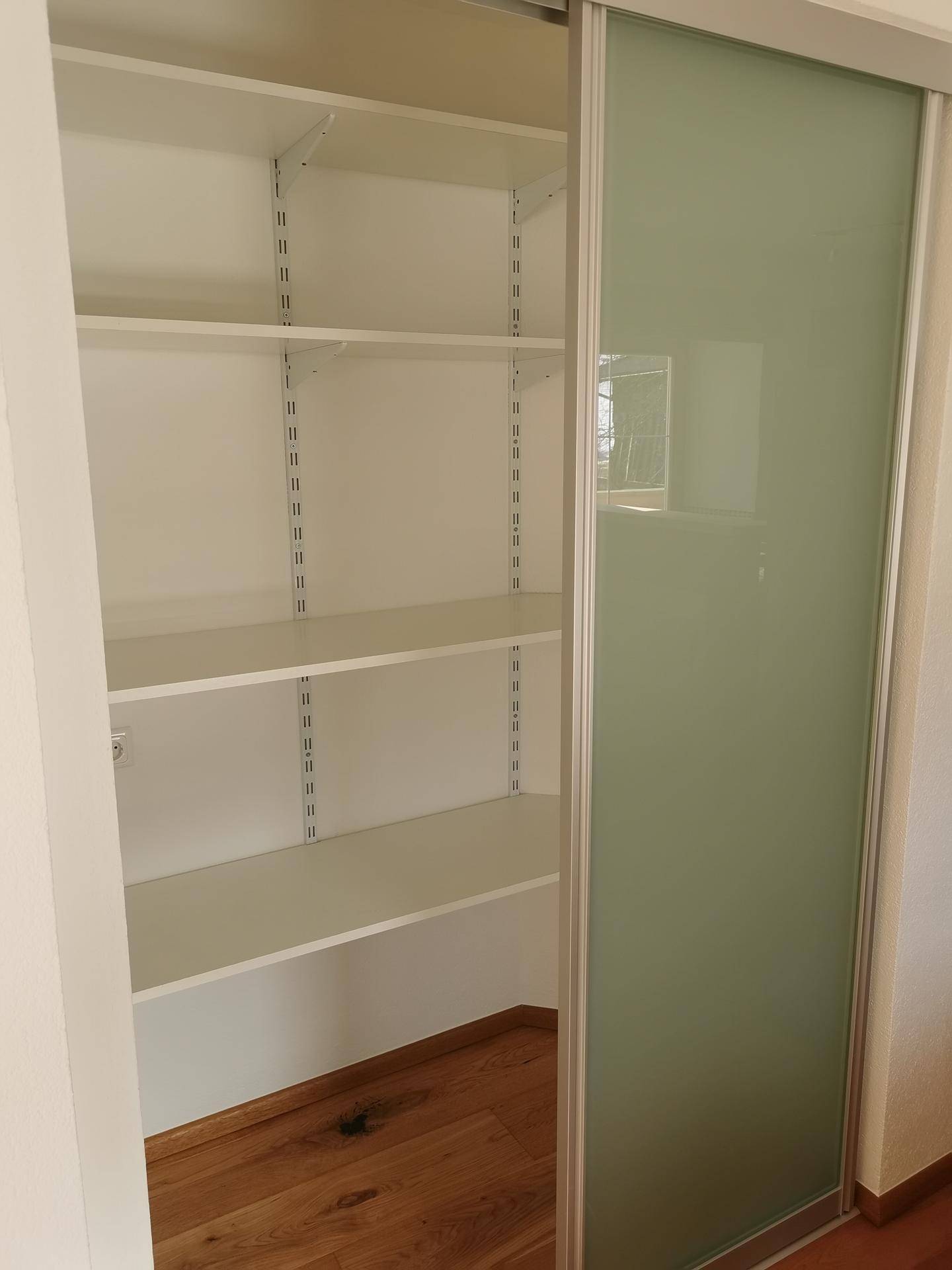 Praktischer Einbauschrank mit mehreren Regalböden und einer Schiebetür aus Milchglas.