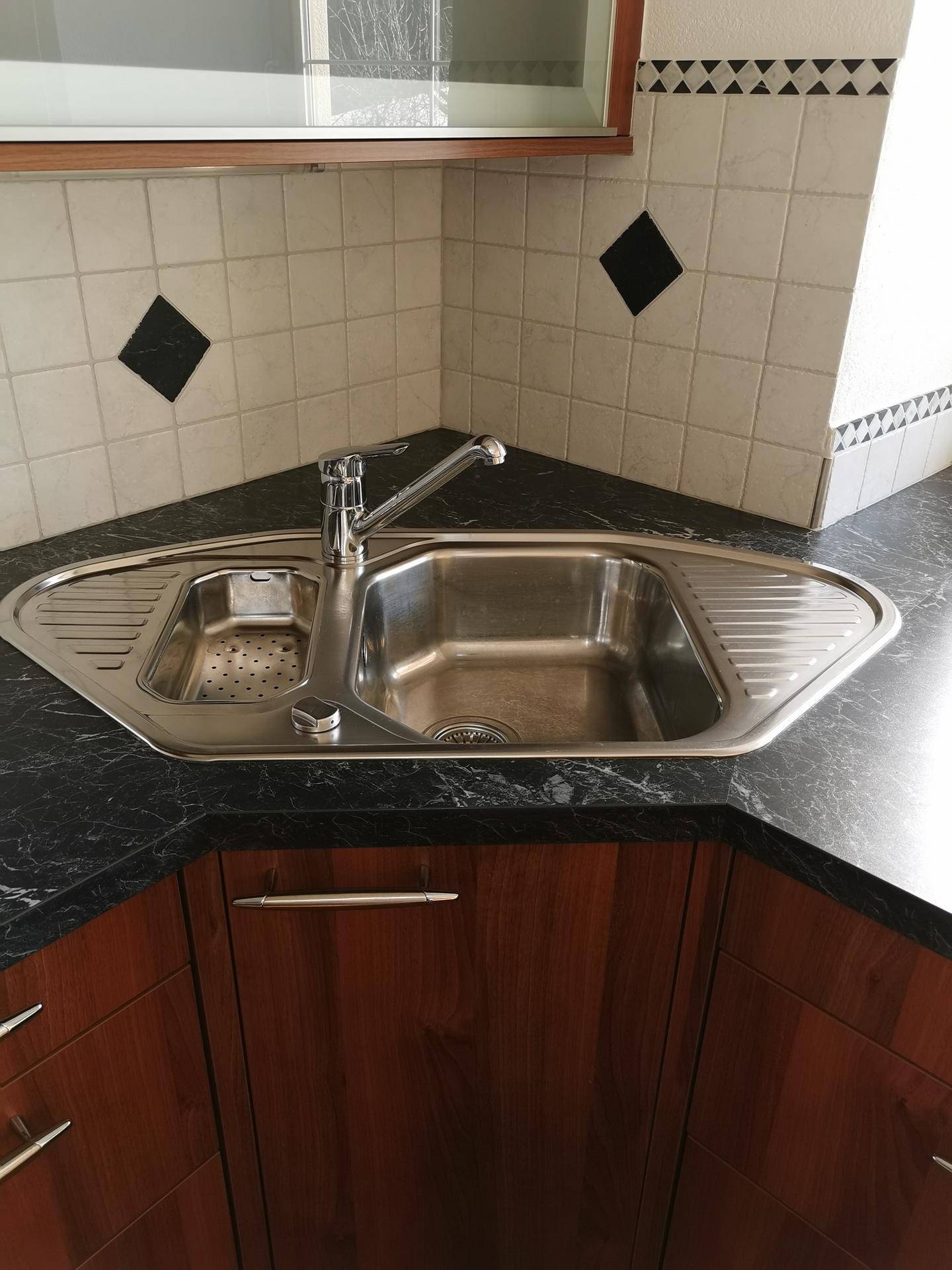 Küchenspüle aus Edelstahl mit dunkler Arbeitsplatte und gefliestem Fliesenspiegel.