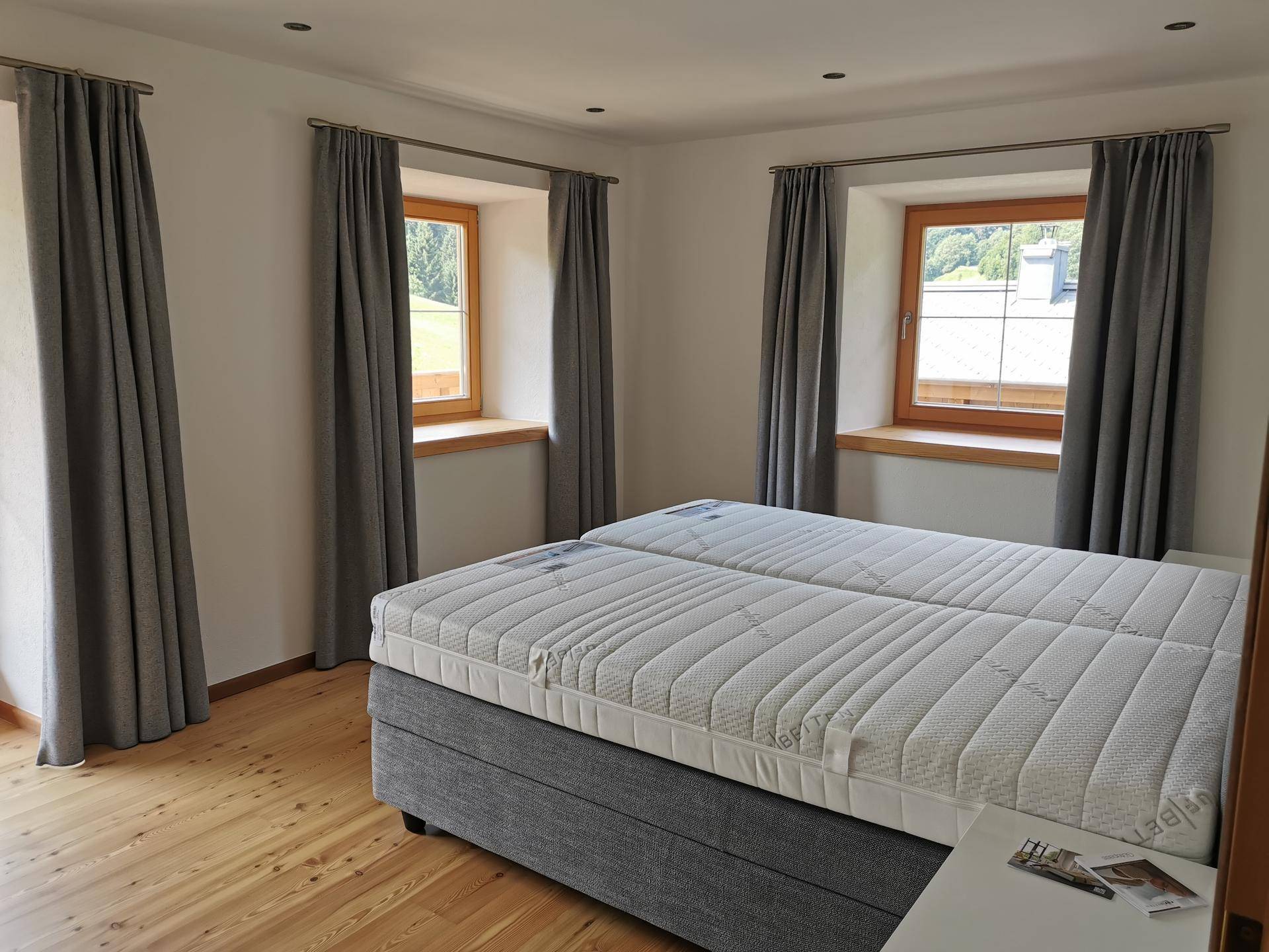 Schlafzimmer mit Doppelbett und Fenstern, die einen schönen Blick ins Grüne bieten.