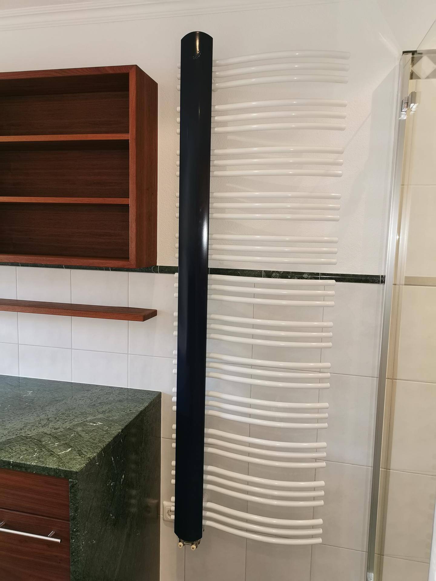 Beheizter Handtuchhalter und Duschbereich mit weißen Wandfliesen im Badezimmer.