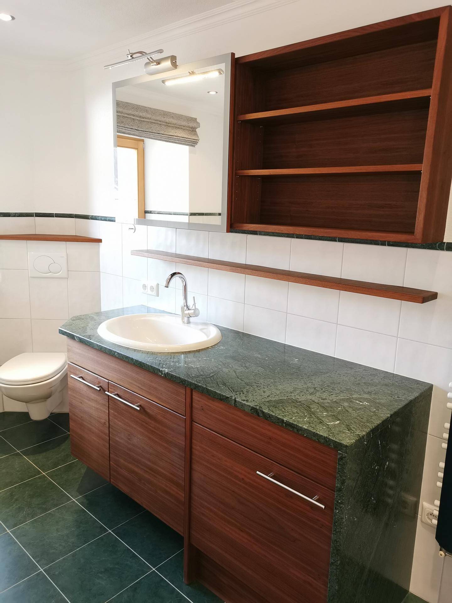 Waschtisch mit Einzelwaschbecken, Spiegel und dunkler Arbeitsplatte im Badezimmer.