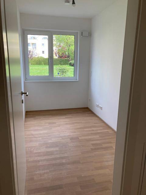 Helles Zimmer mit Holzboden, weißen Wänden und Fenster zum grünen Außenbereich.