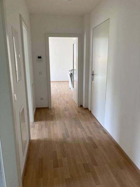 Heller Flur mit Holzboden und weißen Wänden, der zu weiteren Räumen führt.