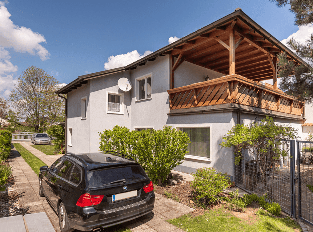 Ansicht des Hauses mit einem überdachten Holzbalkon und einer gepflasterten Einfahrt.