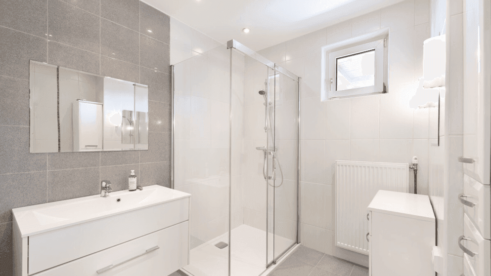 Modernes Badezimmer mit grauen Fliesen, ebenerdiger Dusche und Fenster für Tageslicht.